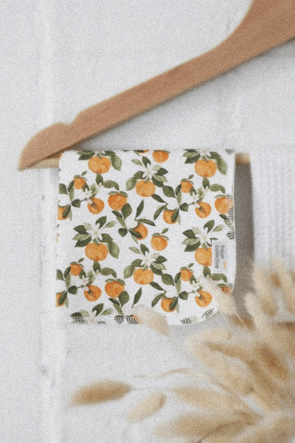 Face cloth showcased in hanger, in Clementine print with various small clementine fruits, white flowers and green leaves