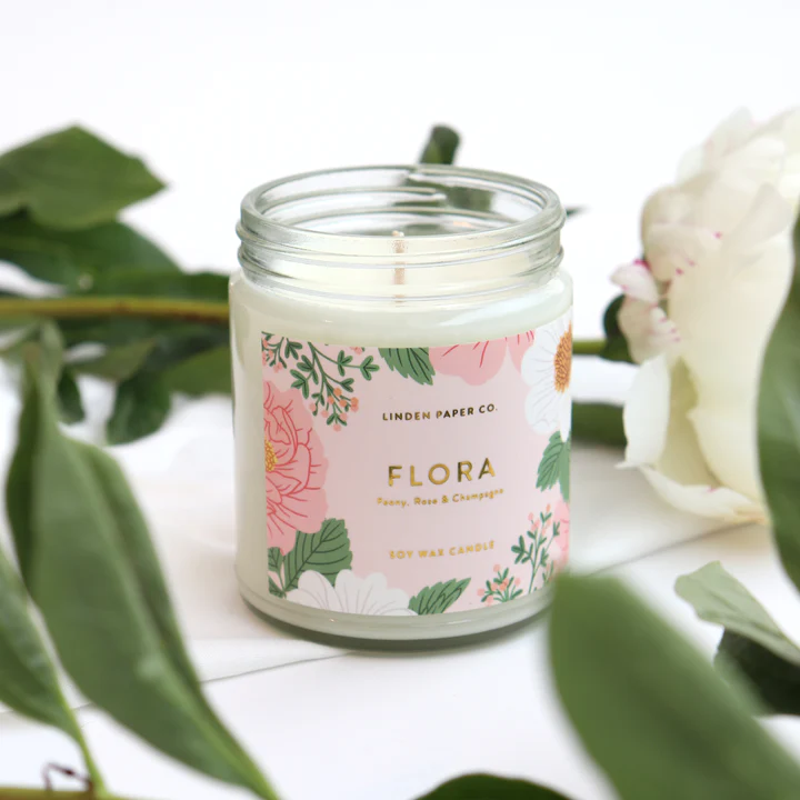 Candle jar and illustrated Flora label printed in full colour with gold foil text, placed beside a white flower