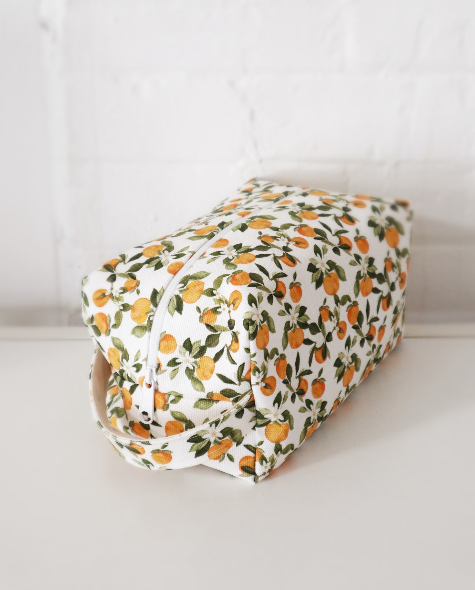 Makeup bag in Clementine print, with various small clementine fruits, white flowers and green leaves